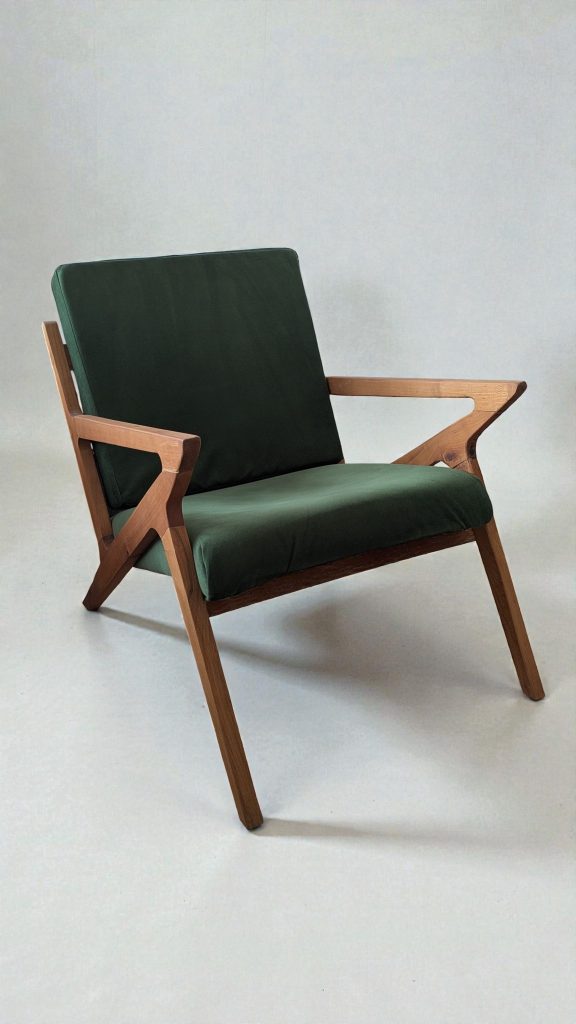 Mid-century wooden armchair with dark green cushions against a pale backdrop.