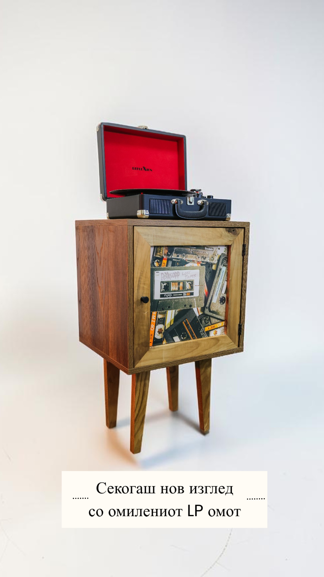 Wooden cabinet on four legs with a red-top vintage vinyl player open on top and a glass-front door showing scattered cassette tapes inside.