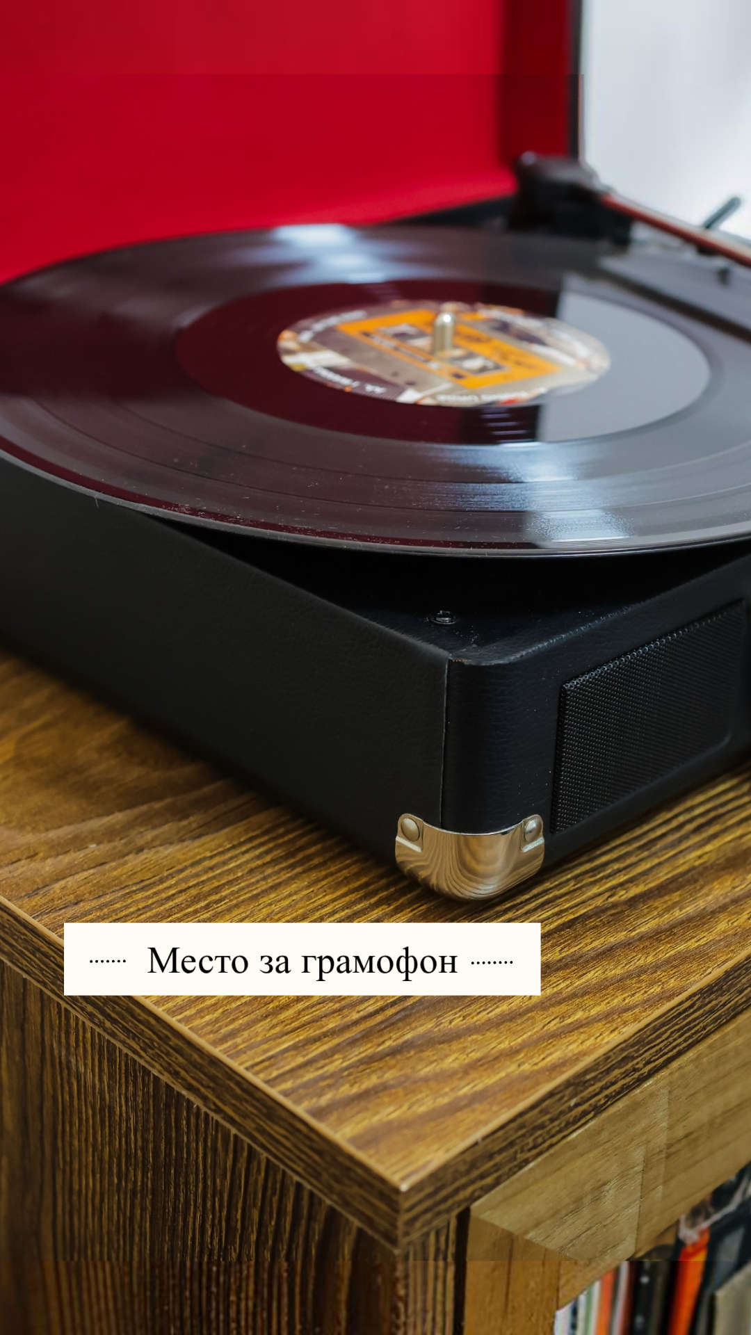 Vinyl record spinning on a black turntable with a red backdrop on a wooden shelf.